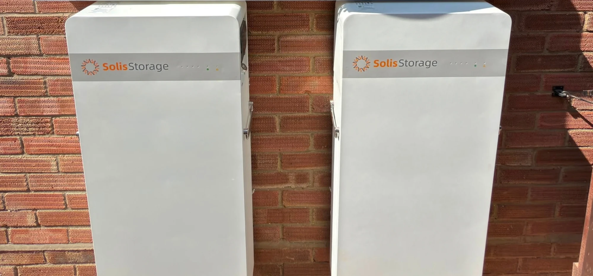 Two Solis Storage batteries mounted on a red brick wall