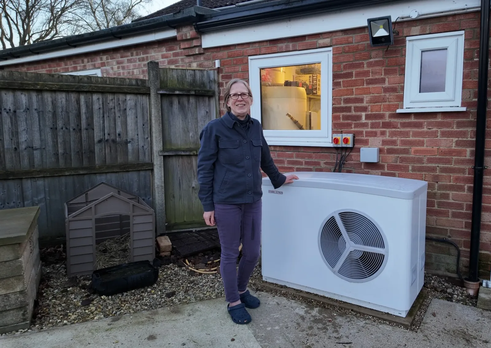 Louise with her Stiebel Eltron air source heat pump beside her red brick home