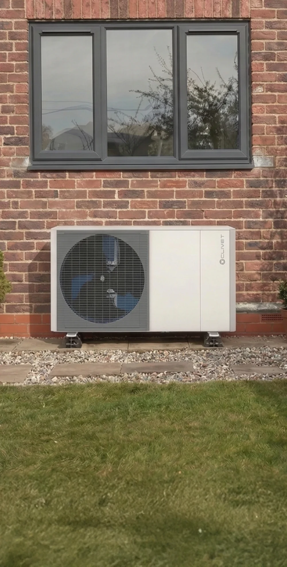 A Clivet heat pump on a red brick wall beneath a grey-framed window