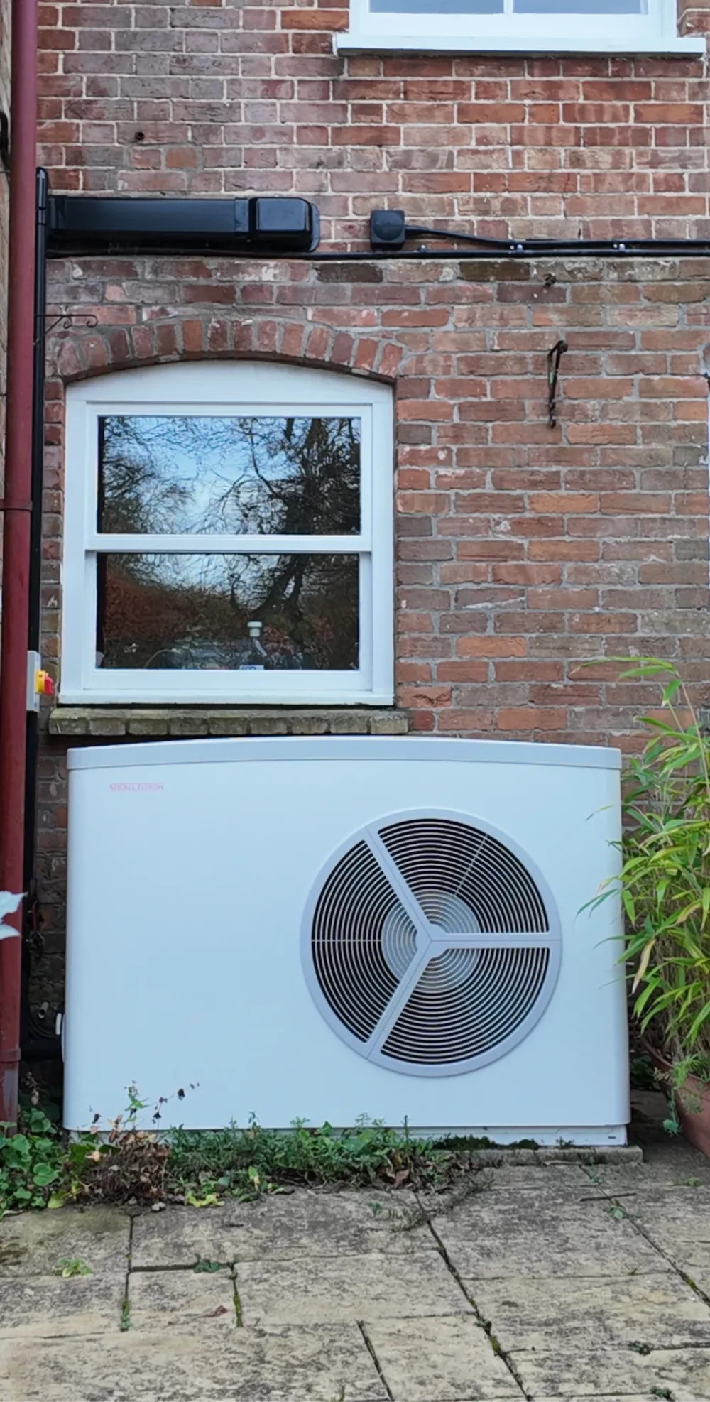 A Stiebel Eltron heat pump beneath a white sash window on an old red-brick wall