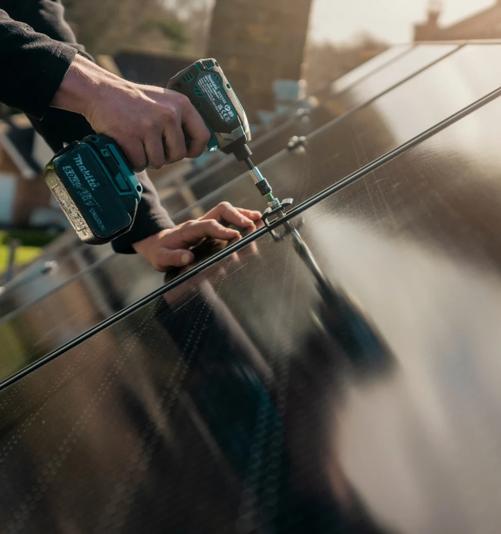 An installer fixing a solar panel to a roof with a cordless drill
