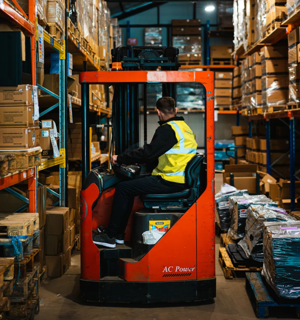 A warehouse operative driving a forklift between stock racks