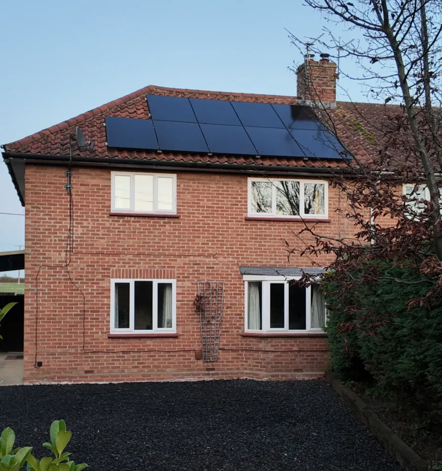 A red-brick semi-detached house with black solar panels on its tiled roof