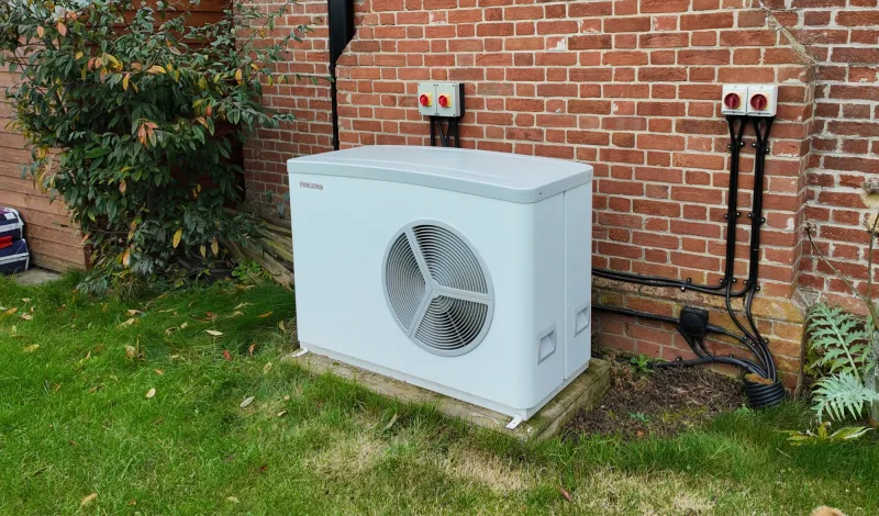 A Stiebel Eltron heat pump on a lawn against red brick, with two sets of isolators above