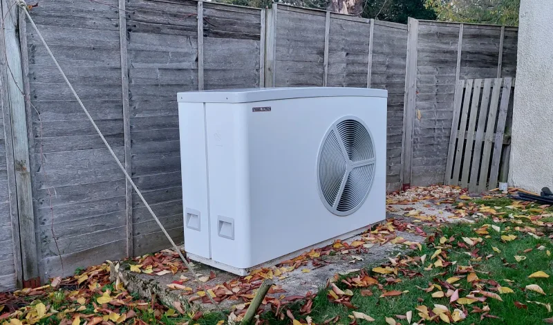 A Stiebel Eltron heat pump against a wooden fence among autumn leaves