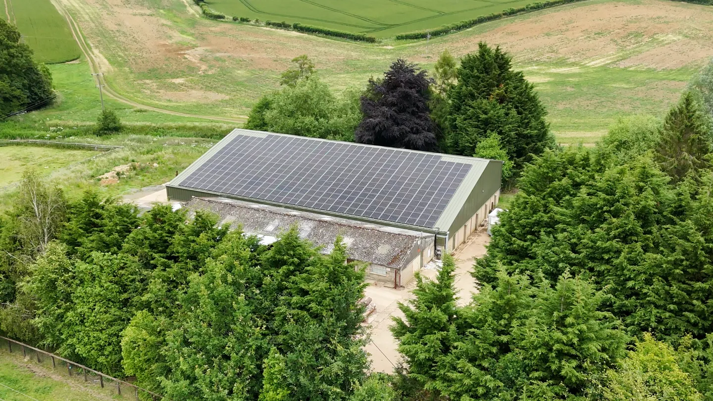 A farm building with solar panels, surrounded by fields