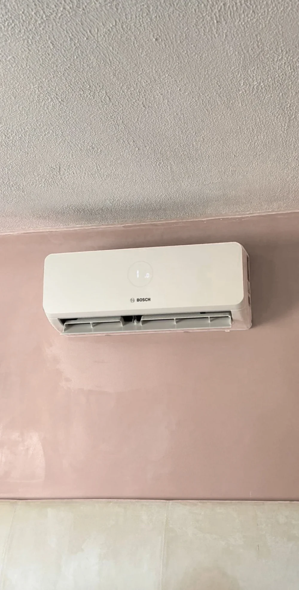 A Bosch wall unit on a pink wall below a textured ceiling