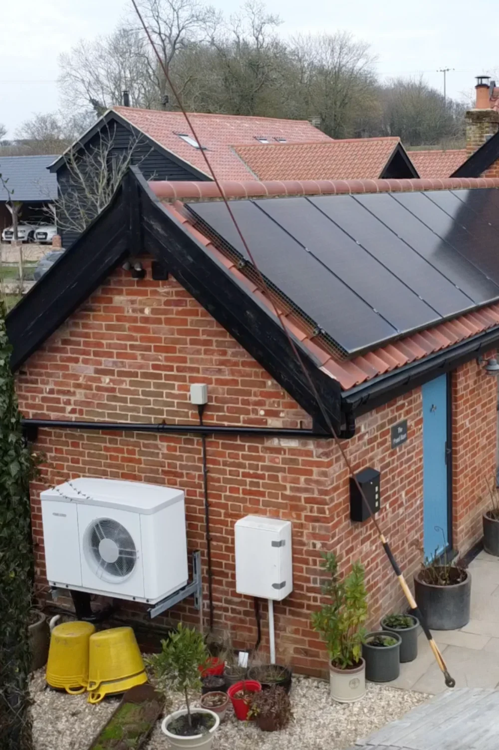 A heat pump and a solar roof on a red-brick cottage with a blue front door