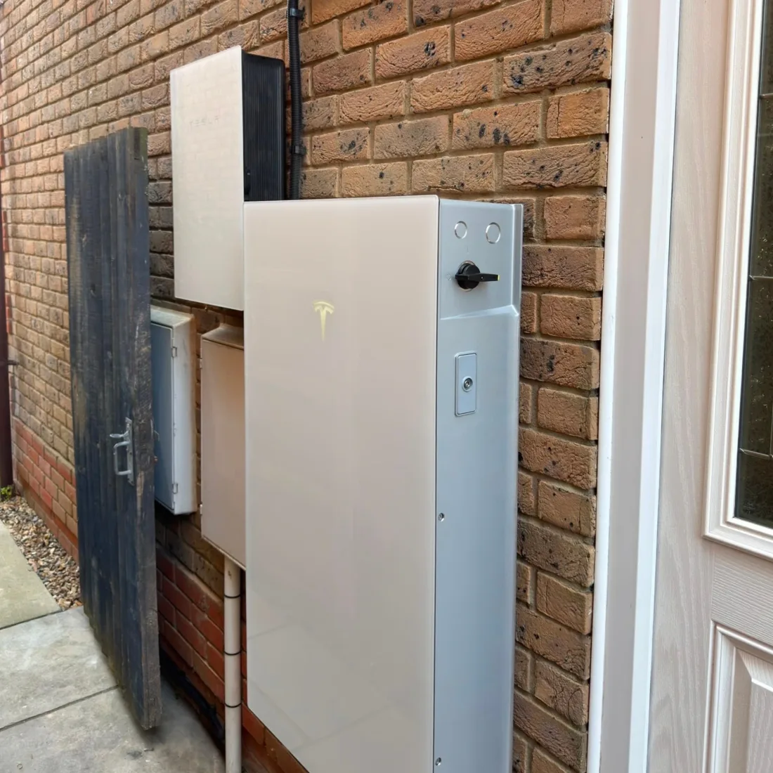 A Tesla Powerwall and gateway on a brick wall beside a front door