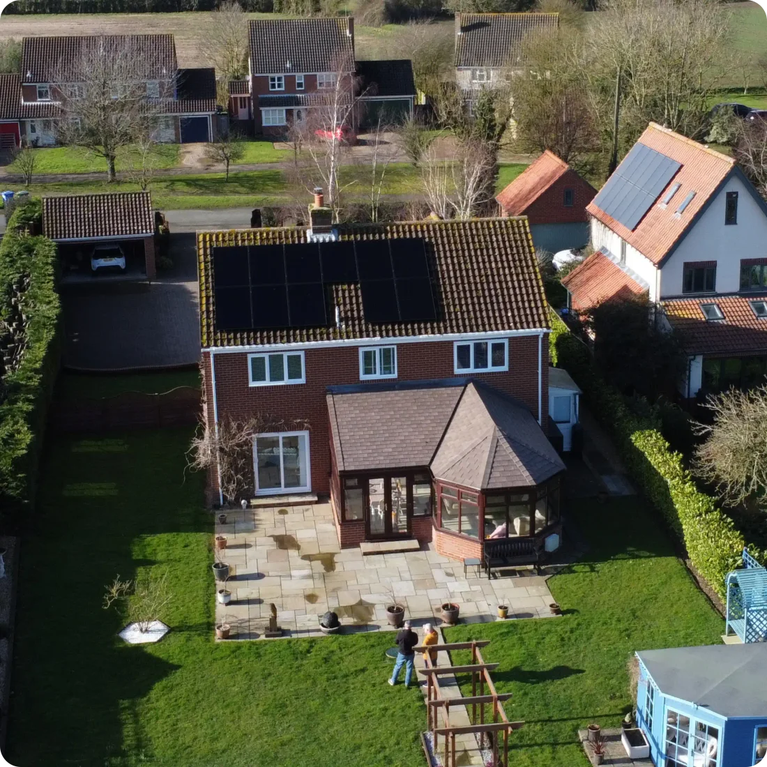 An aerial view of a red-brick house with solar panels on its roof and a large lawn